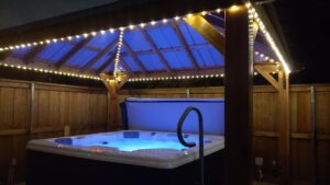 Hot tub with lights under a lighted gazebo in a nighttime setting.