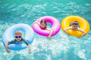 Three kids are hanging out in a pool in colorful floating tubes for a pool party.