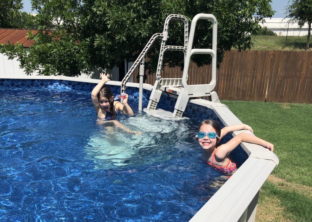 The Best Entry System for Your Above Ground Pool 1 Two girls are standing in an above ground pool. There is a pool ladder system in the background.