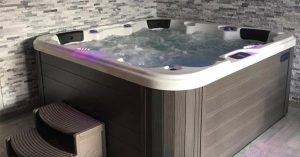 An outdoor hot tub with illuminated water jets, a stone accent wall backdrop, and built-in steps for convenient access.
