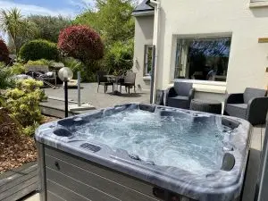 Blogs 1 A hot tub with a gray exterior and foaming water is in a backyard with gray pavers and black patio furniture.