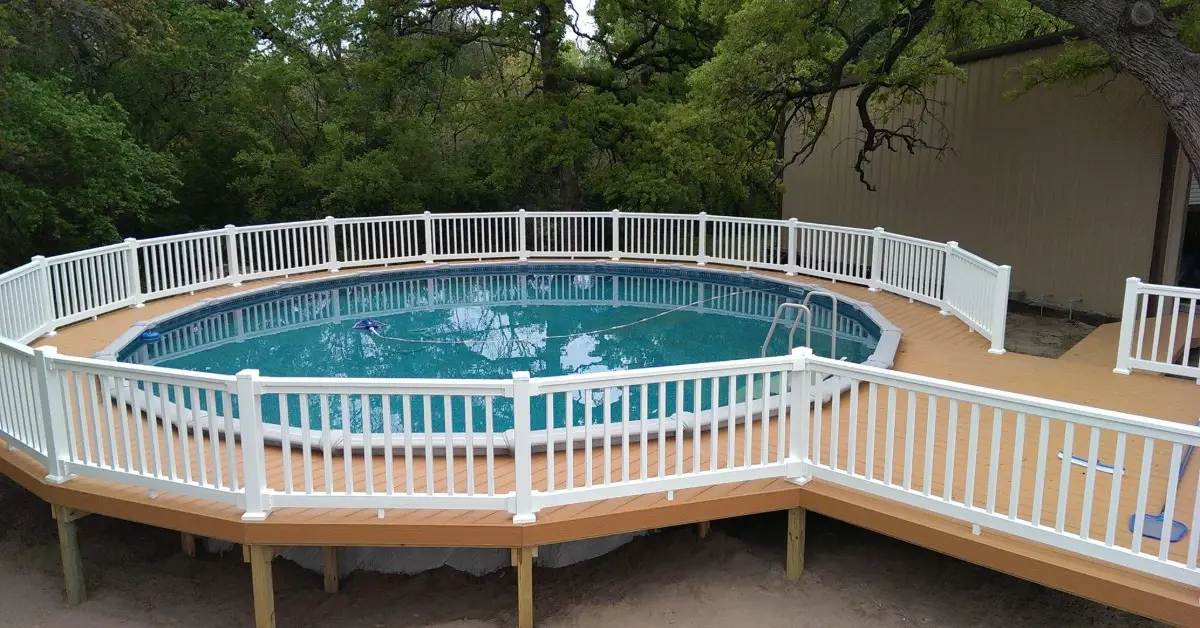 Salt vs. Chlorine Pool Systems: The Differences Explained 1 An above-ground pool is surrounded by a narrow, circular tan deck with a white railing. The pool has a ladder.