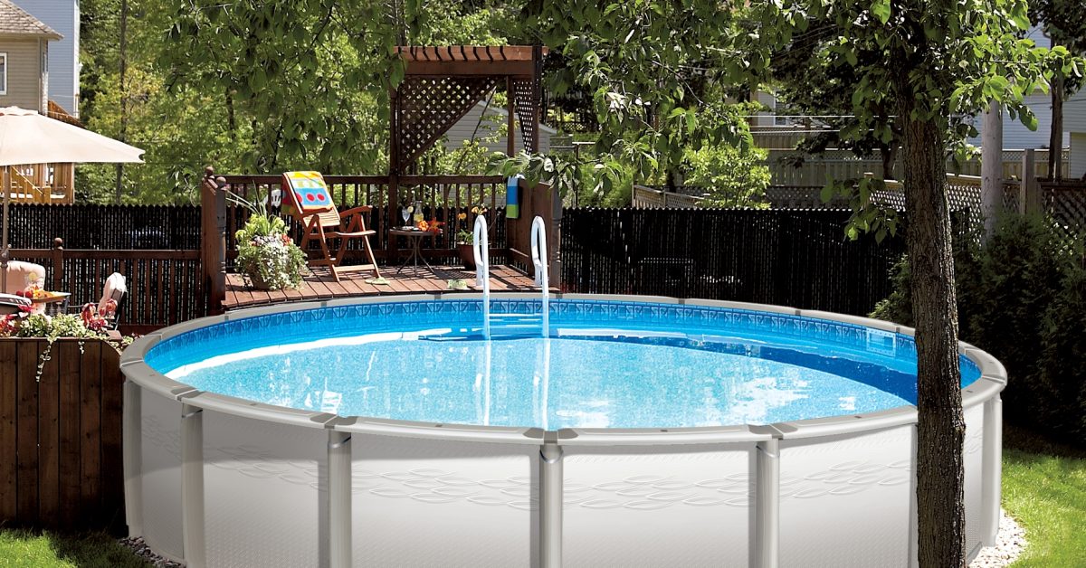 Above-ground pool in a backyard. There is a raised deck against the pool with a lounge chair, side table, and plants.